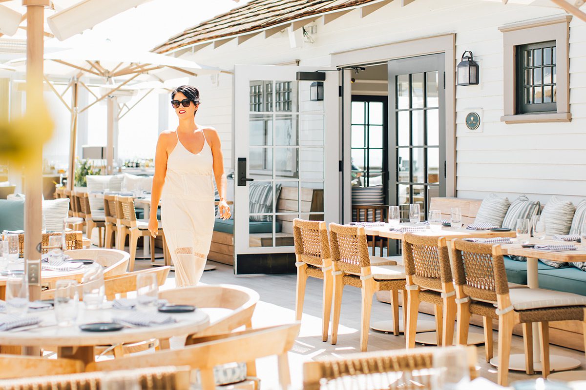 a lady with sunglasses walking by empty tables on the patio
